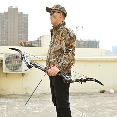 Man in camouflage holding a compound bow on rooftop